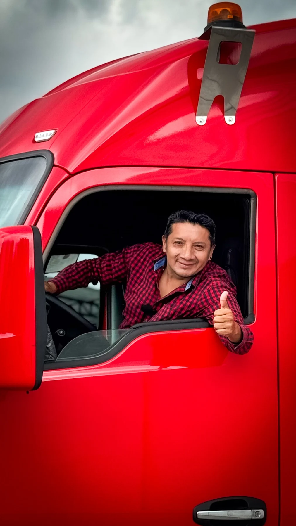 Miguel saludando desde la cabina de un camión rojo
